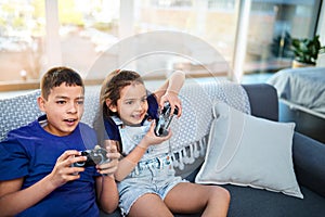 Children, siblings and video game with controller, sofa and online for esports in home. Technology, entertainment and
