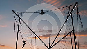 Children silhouettes are jumping on bungee trampoline against twilight sky