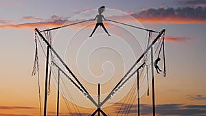 Children silhouettes are jumping on bungee trampoline after sunset: slow motion