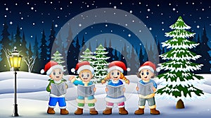 Children singing christmas carols in winter chlotes and santa hat with snowy pine background