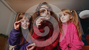 Children sisters girls holding magnifying glass near face, looking into camera, analysing, playing