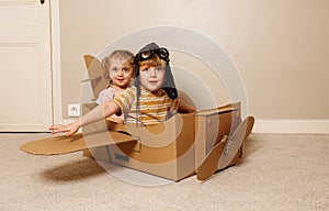 Children sit in cardboard plane wear hat and glasses pretend fly