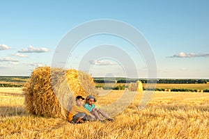 Children sit at a haystack in a field on a sunny day and communicate