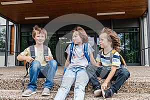 Children sit on the steps of the school and talk. Schoolchildren rest during recess or after school and communicate with