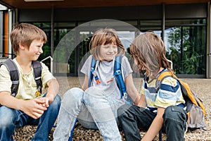 Children sit on the steps of the school and talk. Schoolchildren rest during recess or after school and communicate with