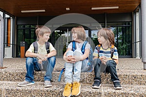 Children sit on the steps of the school and talk. Schoolchildren rest during recess or after school and communicate with