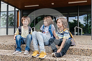 Children sit on the steps of the school and talk. Schoolchildren rest during recess or after school and communicate with