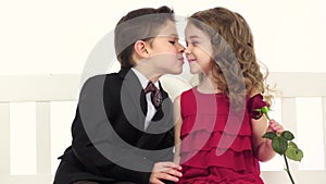 Children sit on a swing and talk, in the girl`s hand a rose. White background. Slow motion. Close up