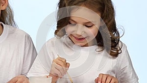 Children sit at the table and decorate the drawings with colors. White background. Slow motion