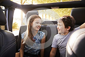 Children Sitting In Back Seat Of Open Top Car On Road Trip