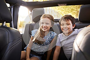 Children Sitting In Back Seat Of Open Top Car On Road Trip