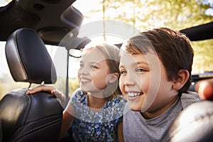 Children Sitting In Back Seat Of Open Top Car On Road Trip