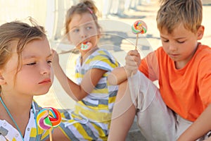 Children sitting on beach and eating lollipops