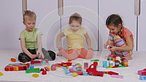 Children sitting on carpet in playroom and playing with constructor lego bricks