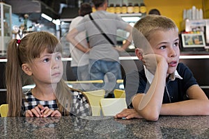 Children sitting in fast food restaurant behind empty table waiting for food