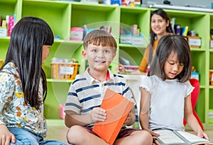 Children sitting on floor and reading tale book in preschool li