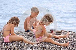 Children sitting on stony beach, creates pyramid