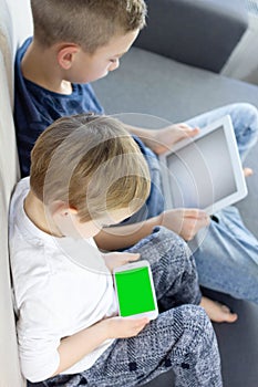 Children sitting and using tablet and mobile smart phone with green screen at home.