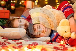 Children sleeping in new year or christmas decoration. Teenage boy and girl. Holiday lights, gifts and christmas tree decorated