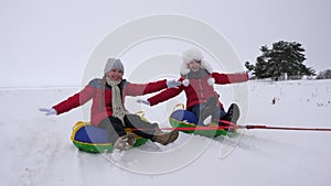 Children slides in snow on an inflatable snow tube and waves hand. Happy girls slides through snow on sled. kids playing