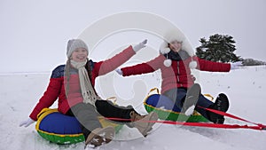 Children slides in snow on an inflatable snow tube and waves hand. Happy girls slides through snow on sled. kids playing