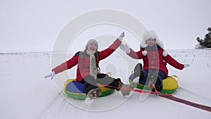 Children slides in snow on an inflatable snow tube and waves hand. Happy girls slides through snow on sled. kids playing