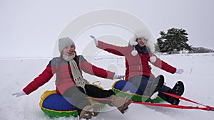 Children slides in snow on an inflatable snow tube and waves hand. Happy girls slides through snow on sled. kids playing