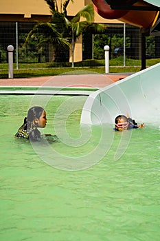 Children sliding into pool after going down water slide during summer