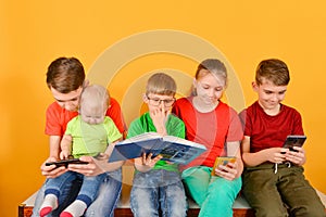 Children with a smartphone are sitting nearby, one boy in glasses is sitting with a book