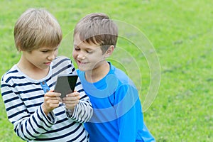 Children with smartphone. Two boys looking to screen, playing games or using application. Outdoor. Technology education