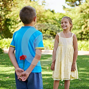 Children, smile and flower in park with surprise for crush, gift or friendship for spring and childhood on grass with