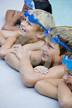 Children smiling, hanging on side of swimming pool