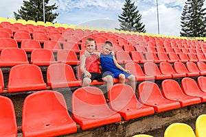 Children in sports uniforms sit on red seats on the sports stand of the stadium. fans