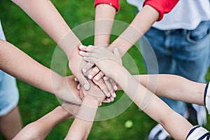 Children stacking hands while standing on green grass