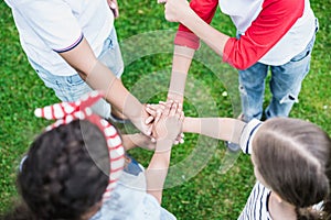 Children stacking hands while standing on green grass