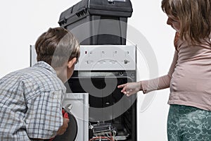 Children stand next to a broken electric stove, the boy has tools in his hands