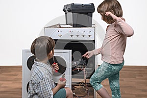 Children stand next to a broken electric stove, the boy has tools in his hands