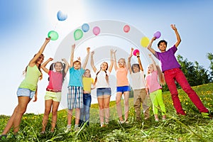 Children standing with arms up to flying balloons
