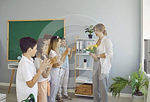 Children students giving flowers to their teacher clapping hands congratulating on holiday.