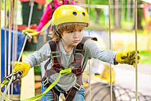 Children summer activities. High ropes walk. Every childhood matters. Happy little boy calling while climbing high tree