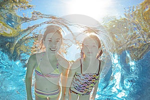 Children swim in pool underwater, girls have fun in water