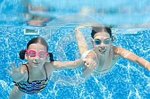 Children swim in swimming pool underwater, little active girls have fun under water, kids fitness and sport