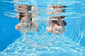 Children swim in swimming pool underwater, little active girls have fun under water, kids sport on family vacation