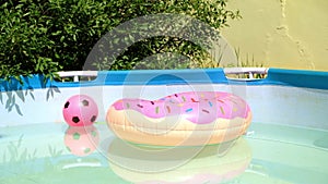 Children swimming pool, pink ball and donut float on sunny summer day. Inflatable pool toy donut in swimming pool on the