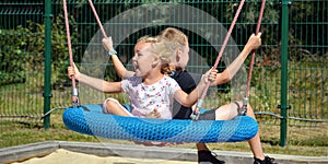 Children on a swing. Boy and girl ride a swing in the park on a summer day. Swing in the children& x27;s amusement park