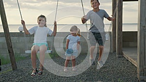 Children swing on a swing in the street at sunset.