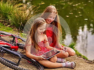 Children with tablet pc near bicycle into river in park .