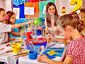 Children with teacher woman painting on paper in kindergarten .