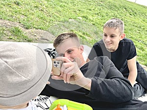 Children and a teenager play taking pictures on the phone while resting in the park