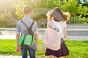 Children teenagers go to school, back view. Outdoors, teens with backpacks.